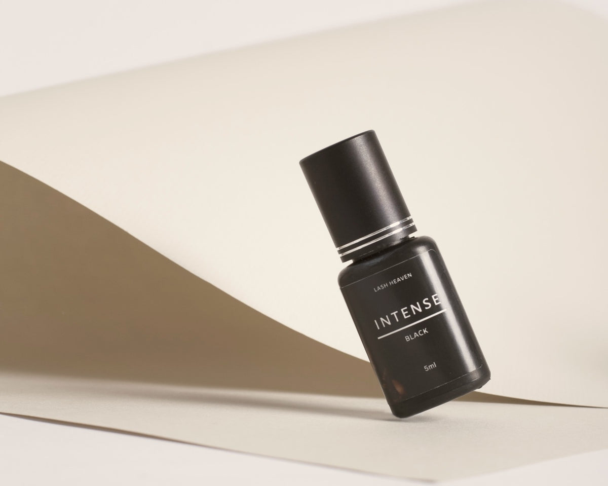Lash Heaven Intense Black lash adhesive on folded ivory and taupe paper